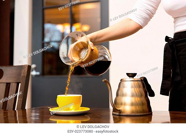 equipment, coffee shop, people and technology concept - close up of barista woman with glass coffeemaker and pot pouring hot coffee to cup at cafe bar or...