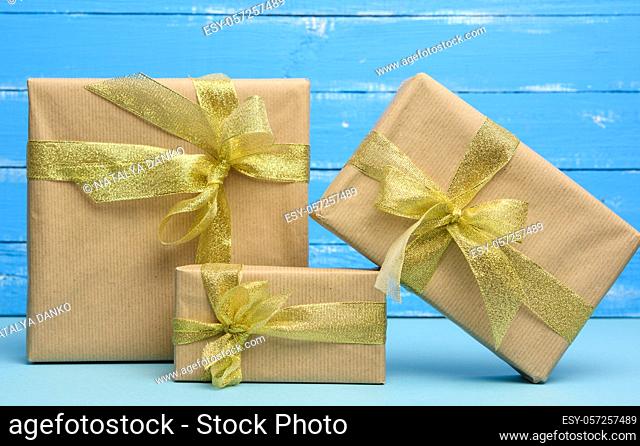 stack of gifts wrapped in brown kraft paper and tied with golden ribbon, boxes on a blue background