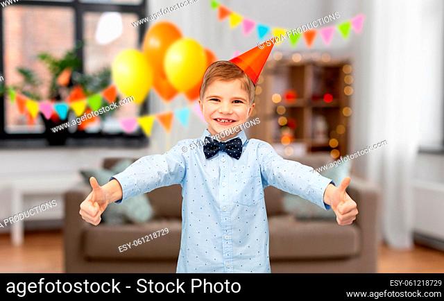 happy boy in birthday party hat showing thumbs up