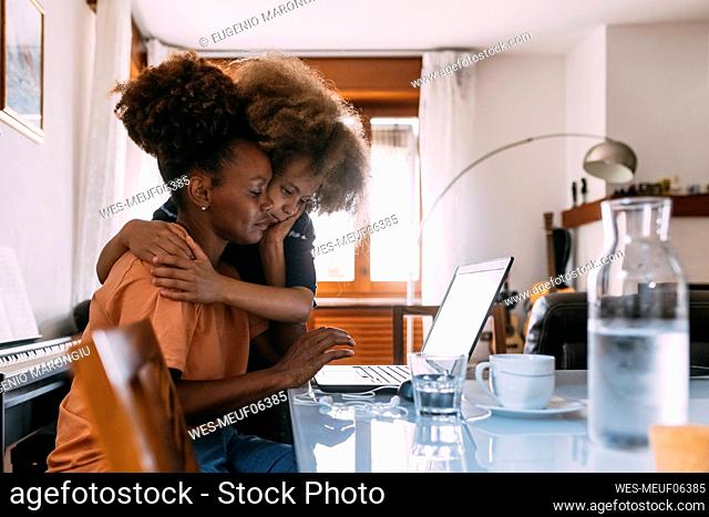 Businesswoman using laptop and embracing son at home