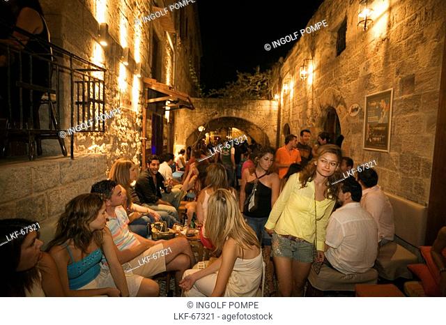 People sitting in outdoor areas of several bars of old town, Rhodes Town, Rhodes, Greece, Since 1988 part of the UNESCO World Heritage Site