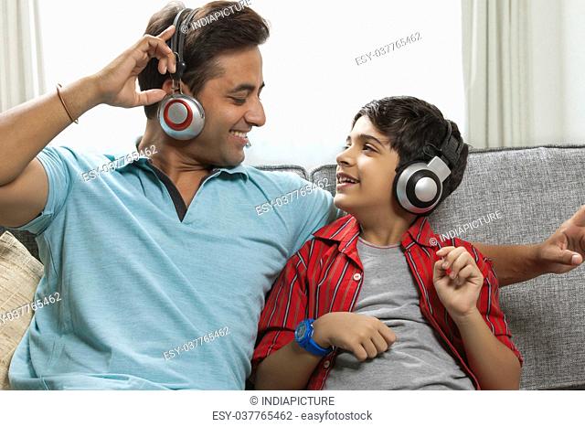 Father and son listening to music together on sofa with headphones