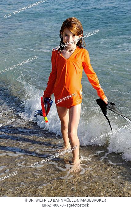 Girl with snorkeling gear, flippers and goggles on a beach by the sea