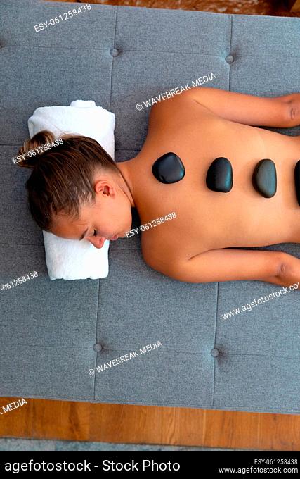 Caucasian young woman with eyes closed receiving hot stone massage at home
