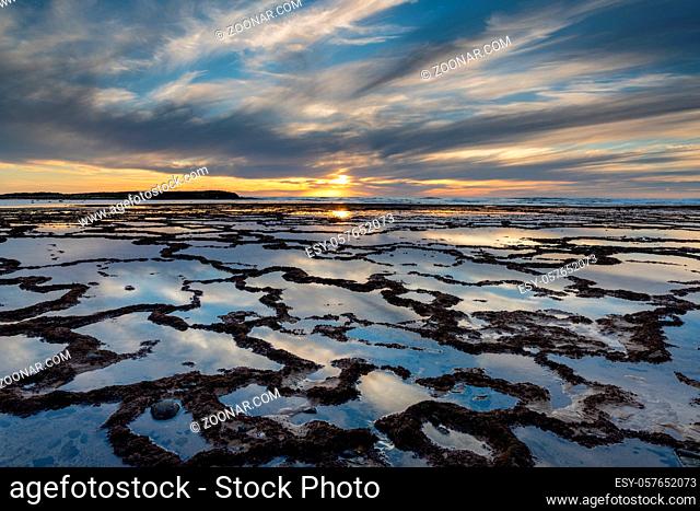 A beautiful sunset over the ocean with rocky beach and tidal pools in the foreground