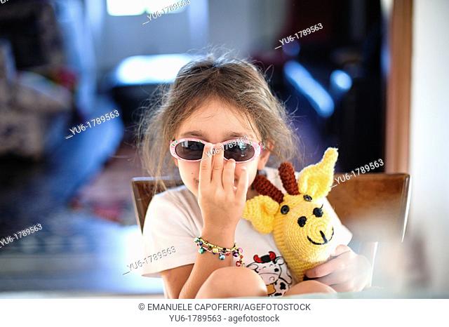 Little girl plays with glasses sitting at the kitchen table