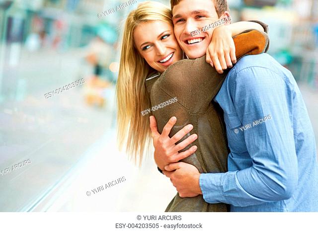 Happy young couple embracing on the sidewalk in front of shop windows