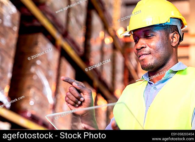 Portrait of african black warehouse worker hold tablet and touch on virtual screen in front of him in large warehouse distribution environment