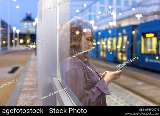 Woman using smart phone seen through glass at tram station