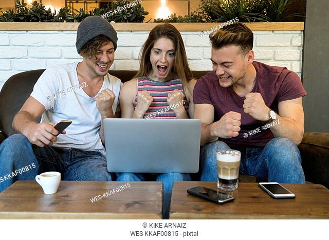 Three excited friends looking at laptop in a cafe