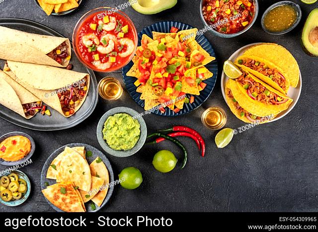 Mexican food, many dishes of the cuisine of Mexico, flat lay, overhead shot on a black background with copy space. Nachos, tequila, guacamole, burritos