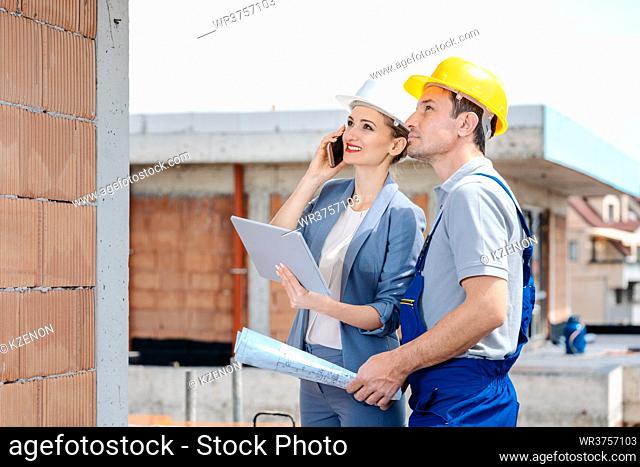 Project developer and construction worker on site using technology like phone and tablet computer
