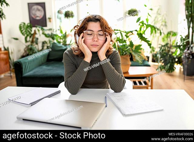 Freelancer with eyes closed sitting on table at home