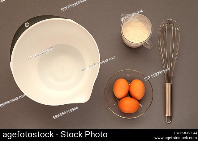 Whisk and a plastic cup for whipping on a gray background. Dishes for the preparation of whipped products