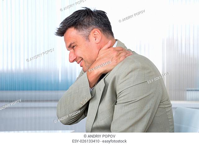 Side view of businessman suffering from shoulder pain in office