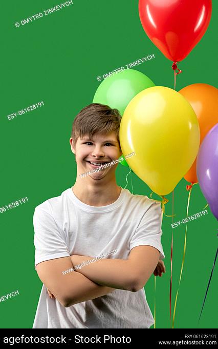 Waist-up portrait of a joyful teenager with Down syndrome posing against the bright colorful balloons