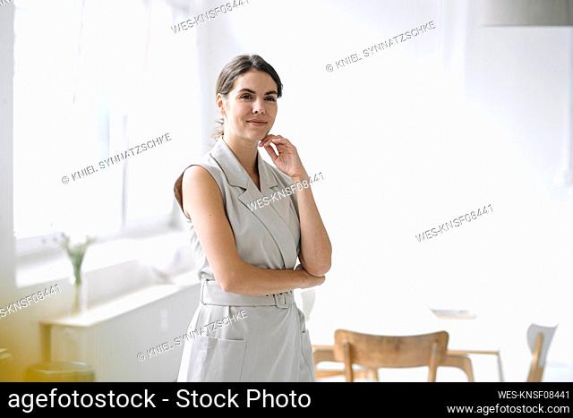 Beautiful businesswoman with hand on chin standing at office