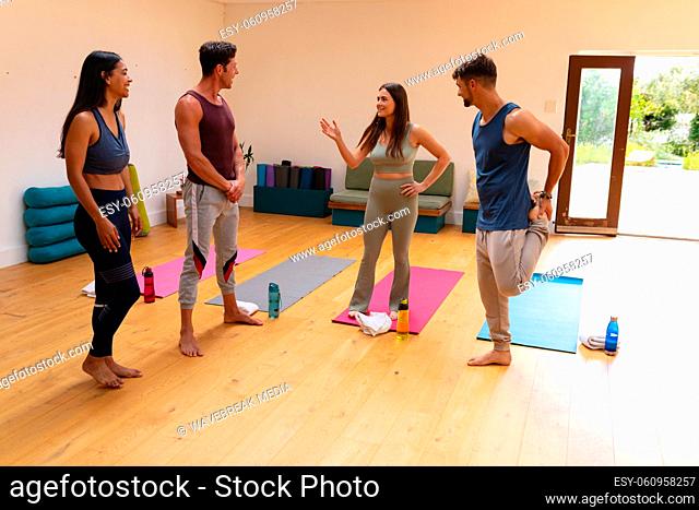 Multiracial male and female friends talking while standing on hardwood floor in yoga studio