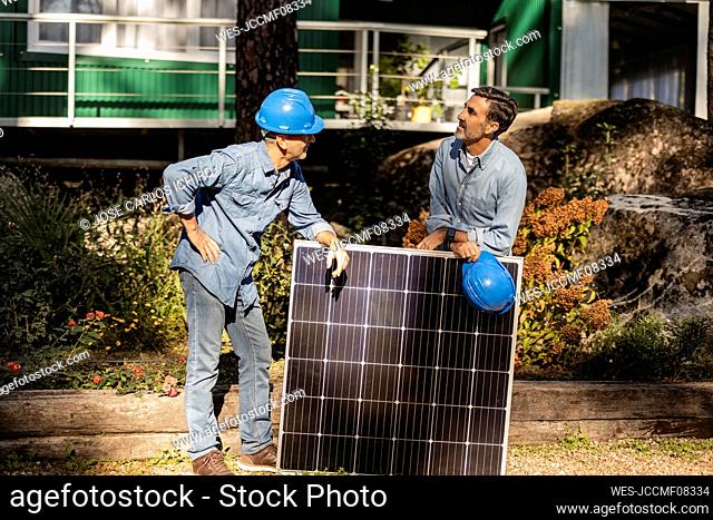 Talking photovoltaic technicians leaning on solar panel