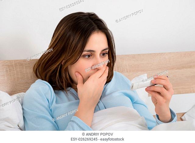 Worried Young Woman Checking Pregnancy Test On Bed
