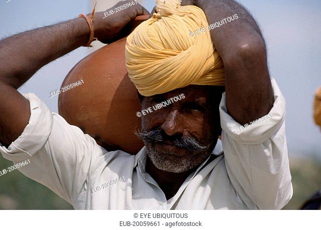 Bhansda Village. Portrait of desert man wearing yellow turban and carrying water vessel on his shoulder