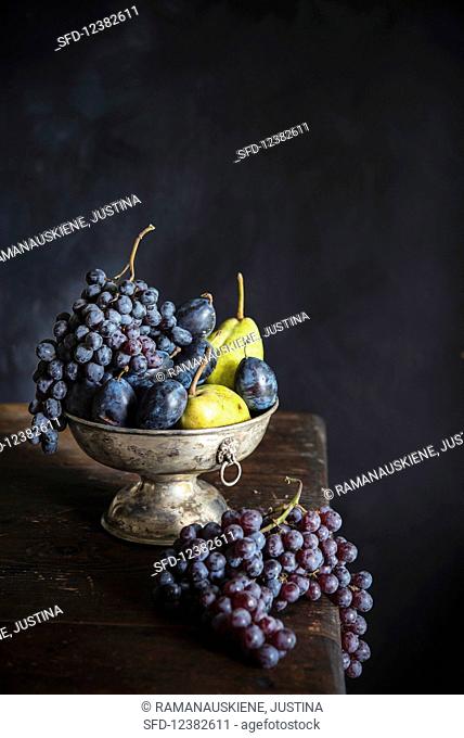 Grapes, plums and pears in a metal bowl on a wooden table