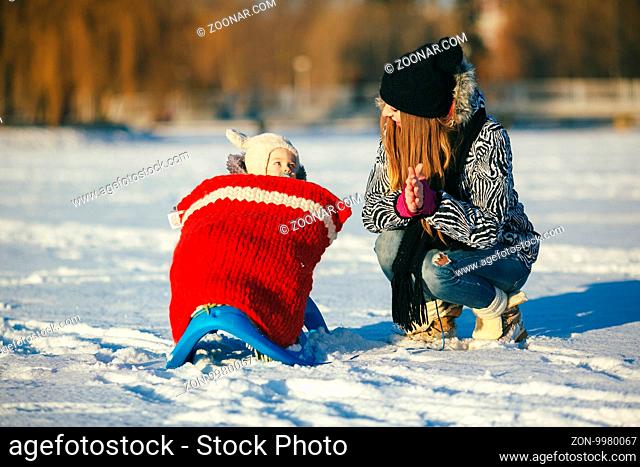 happy family mother and baby girl daughter playing in winter outdoors in the snow