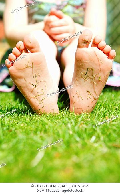 Four year old girl in a garden with grass cuttings on the soles of her feet