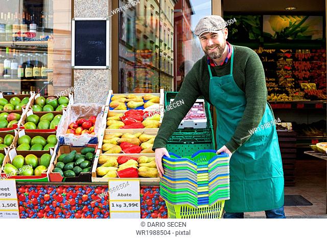 Grocer arranging shopper baskets in front of greengrocer's shop