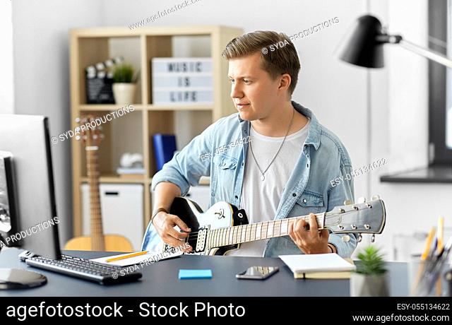 young man with computer playing guitar at home