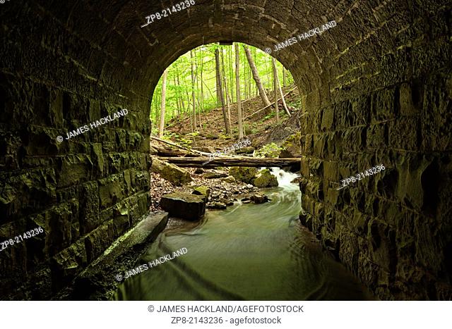 The entrance of a lovely stone block culvert looking out towards the forest in Tiffany Falls Conservation Area, Hamilton, Ontario, Canada