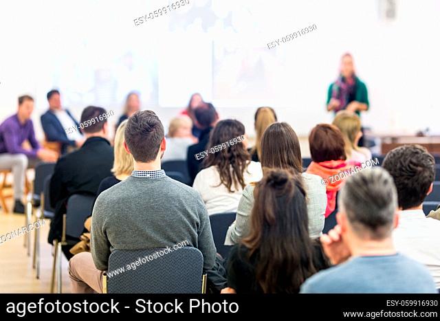 Business and entrepreneurship symposium. Female speaker giving a talk at business meeting. Audience in conference hall. Rear view of unrecognized participant in...