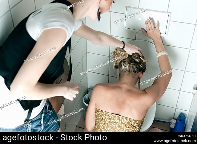 Woman had too many drinks and is drunk and is throwing up in the toilet, a friend is helping her