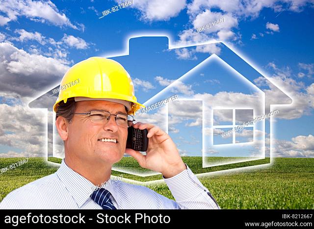 Contractor in hardhat on his cell phone over house icon, empty grass field and deep blue sky with clouds