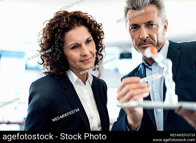 Businessman checking robot arm while standing by colleague in industry