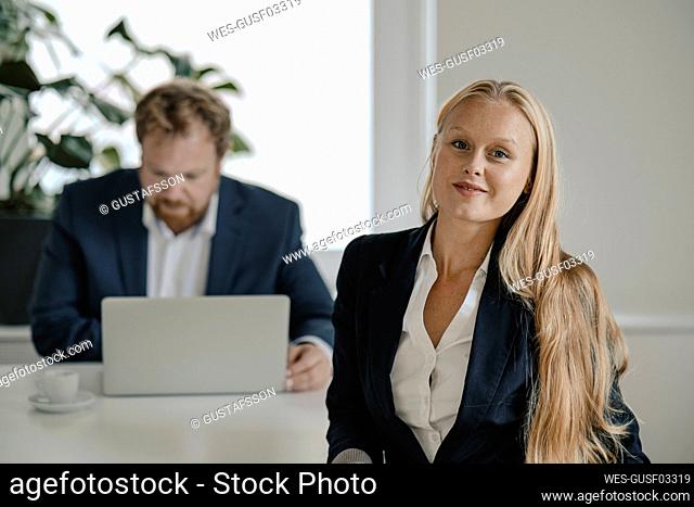 Portrait of confident businesswoman in office with businessman in background