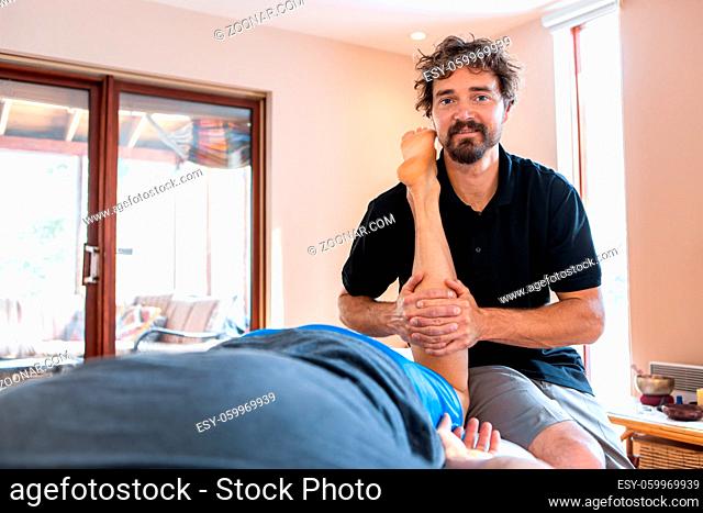 A sportsman receiving treating massage at home. Therapeutic body massage treatment. Osteopathy and sports injury rehabilitation concepts