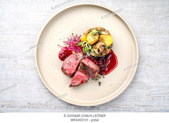 Traditional barbecue dry aged sliced venison fillet steak with potato mushroom terrine and cowberry sauce as top view on a plate with copy space