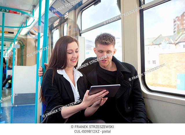 Businesswoman and businessman using digital tablet in Docklands Light Railway train, London