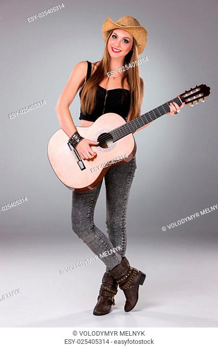 The beautiful girl in a cowboy's hat playing acoustic guitar on a gray background. Portrait in full growth