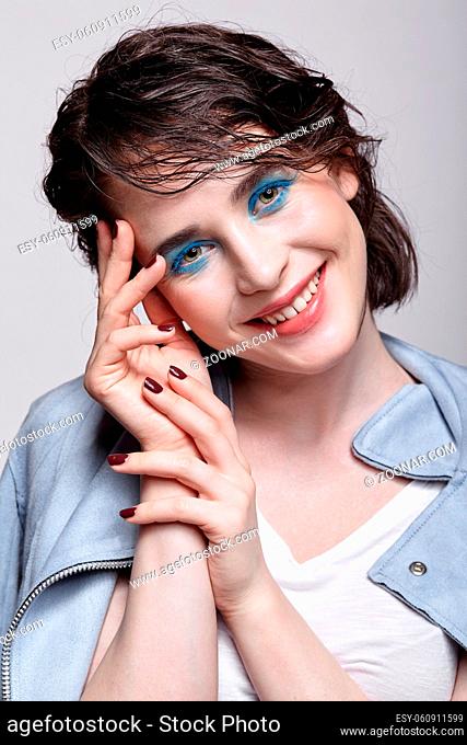 Portrait of smiling female in blue jacket. Woman with unusual beauty makeup and wet hair. Girl with perfect skin, green pistachio colour eyes and blue shadows...
