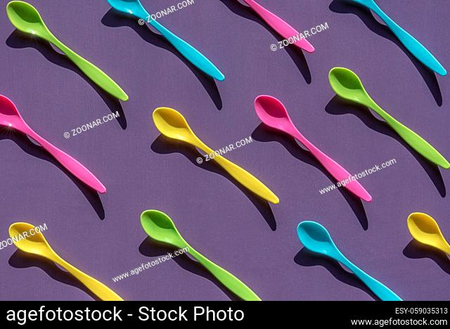 Gastronomy banner idea with a bunch of plastic small spoons, in various vibrant colors, arranged symmetrically, on a purple wooden background
