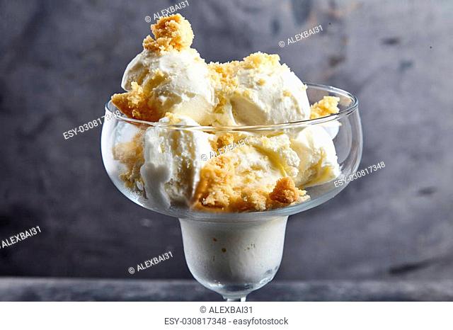 Delicious homemade vanilla ice cream with crumbs of shortbread in glass ice cream bowl with dessert spoon. Cookies made from semolina with sugar crust next to...