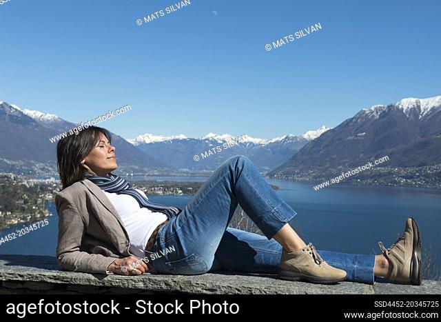 Woman Lying and Enjoy the Panoramic View over Alpine Lake Maggiore with Snow-capped Mountain in Ascona, Switzerland