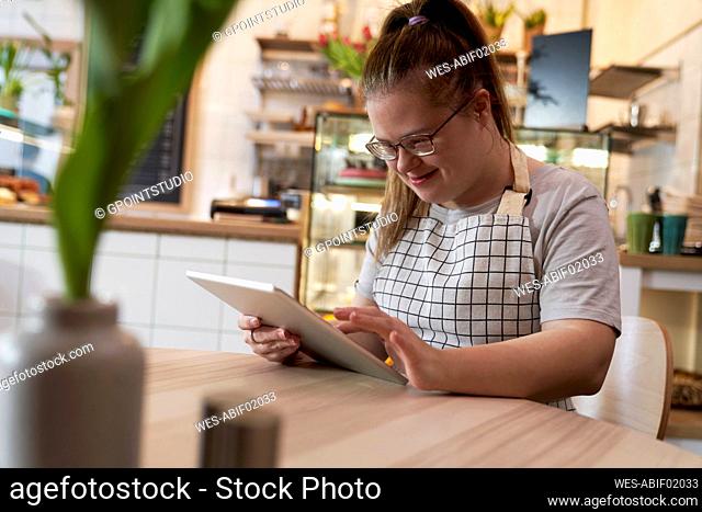 Smiling cafe owner with down syndrome using tablet PC at table in coffee shop