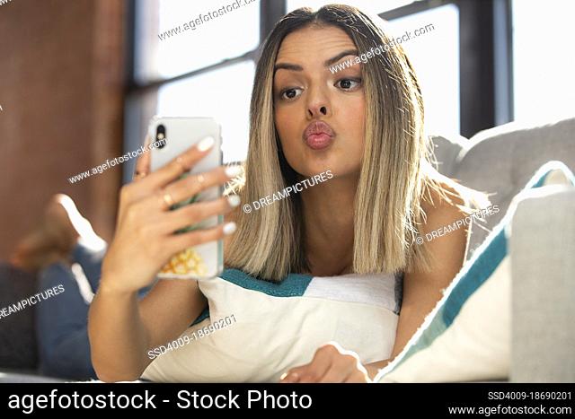 Portrait of a young girl laying on a sofa with a mobile phone taking a selfie with pursed lips