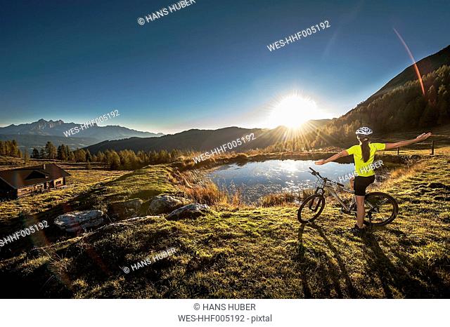 Austria, Altenmarkt-Zauchensee, young woman with mountain bike in the mountains at sunrise
