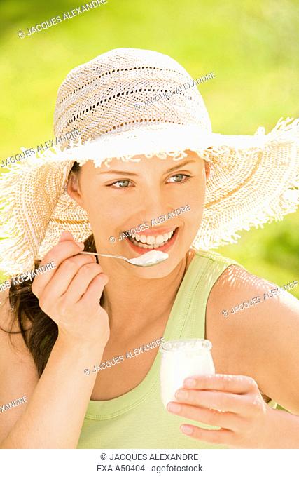 Young woman with a straw hat eating yoghurt