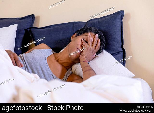 Woman covering face and lying on bed at home