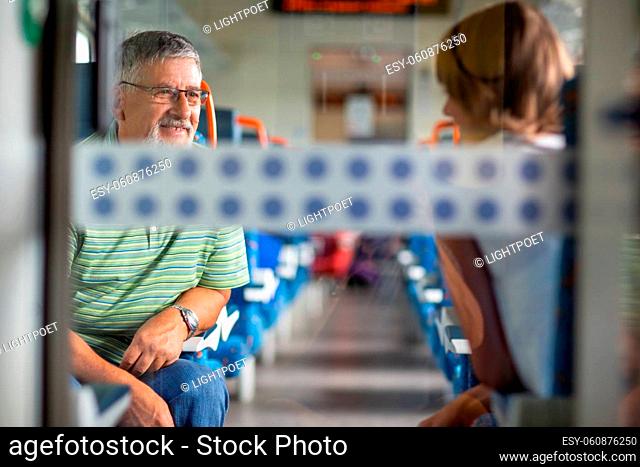 Senior man enjoying a train travel - leaving his car at home, he savours the time spent travelling, talking to other passangers on board